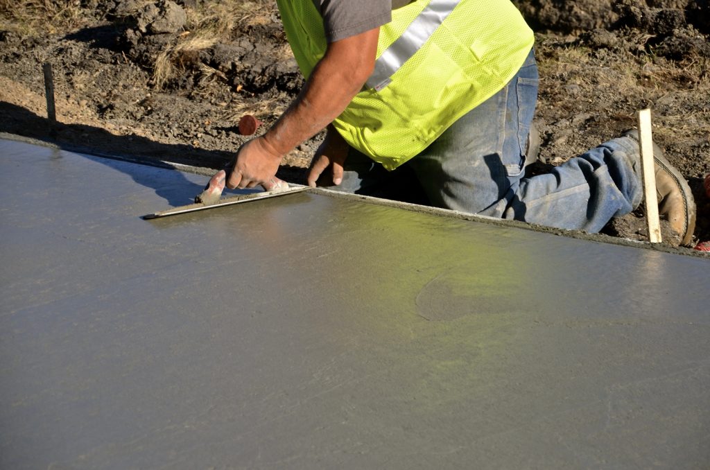 Construction worker troweling wet concrete on a sidewalk project